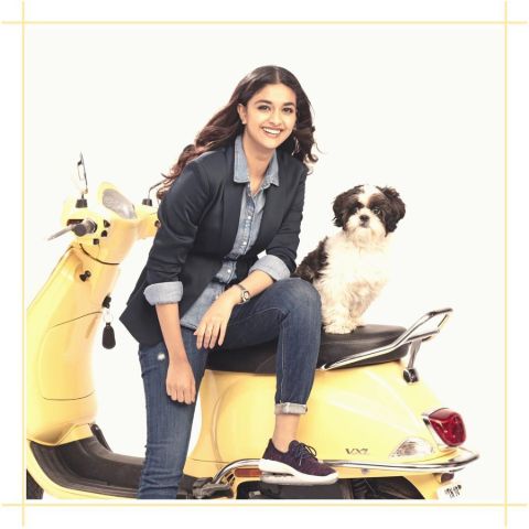 Keerthy Suresh in a black suit poses a picture with a dog in a photoshoot.